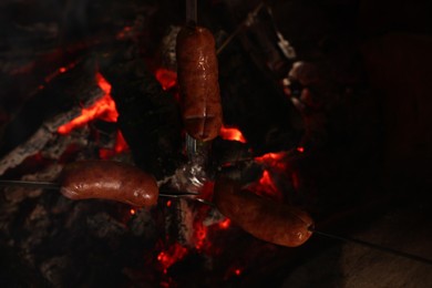 Roasting sausages on campfire outdoors at night, closeup