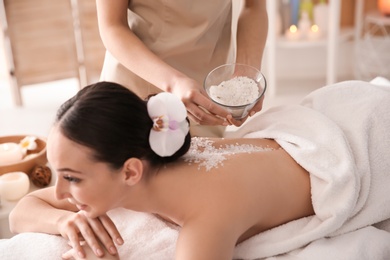 Beautiful young woman having massage with body scrub in spa salon