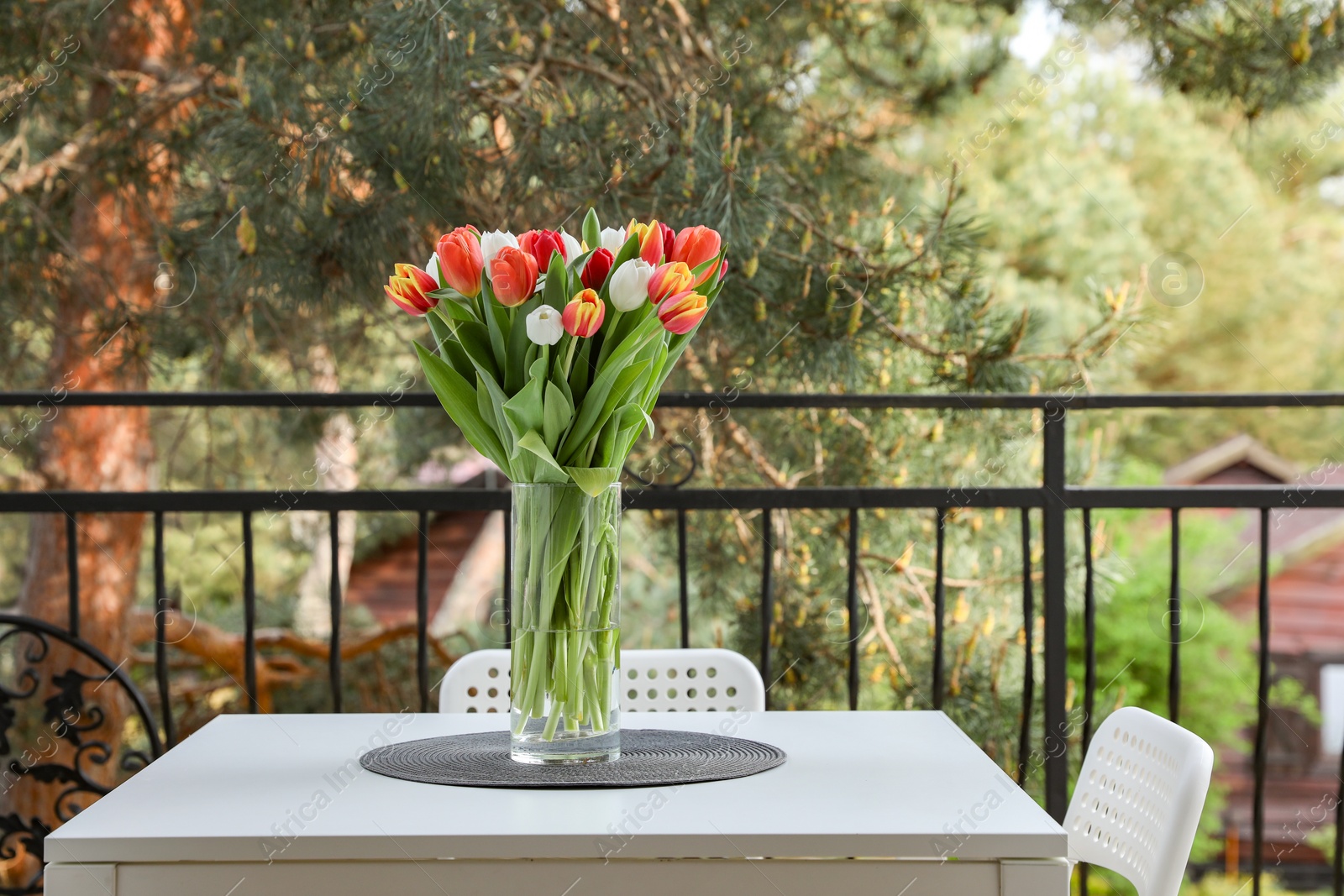Photo of Beautiful colorful tulips in glass vase on white table at balcony, space for text