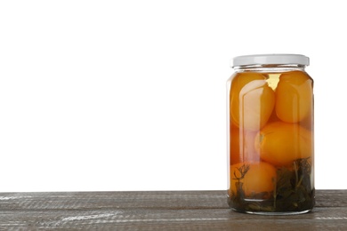 Photo of Jar of pickled yellow tomatoes on wooden table against white background. Space for text