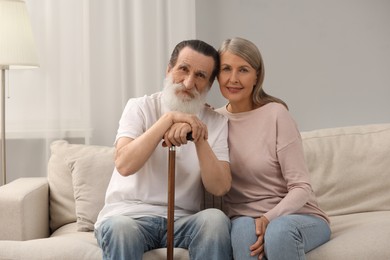 Senior man with walking cane and mature woman on sofa at home