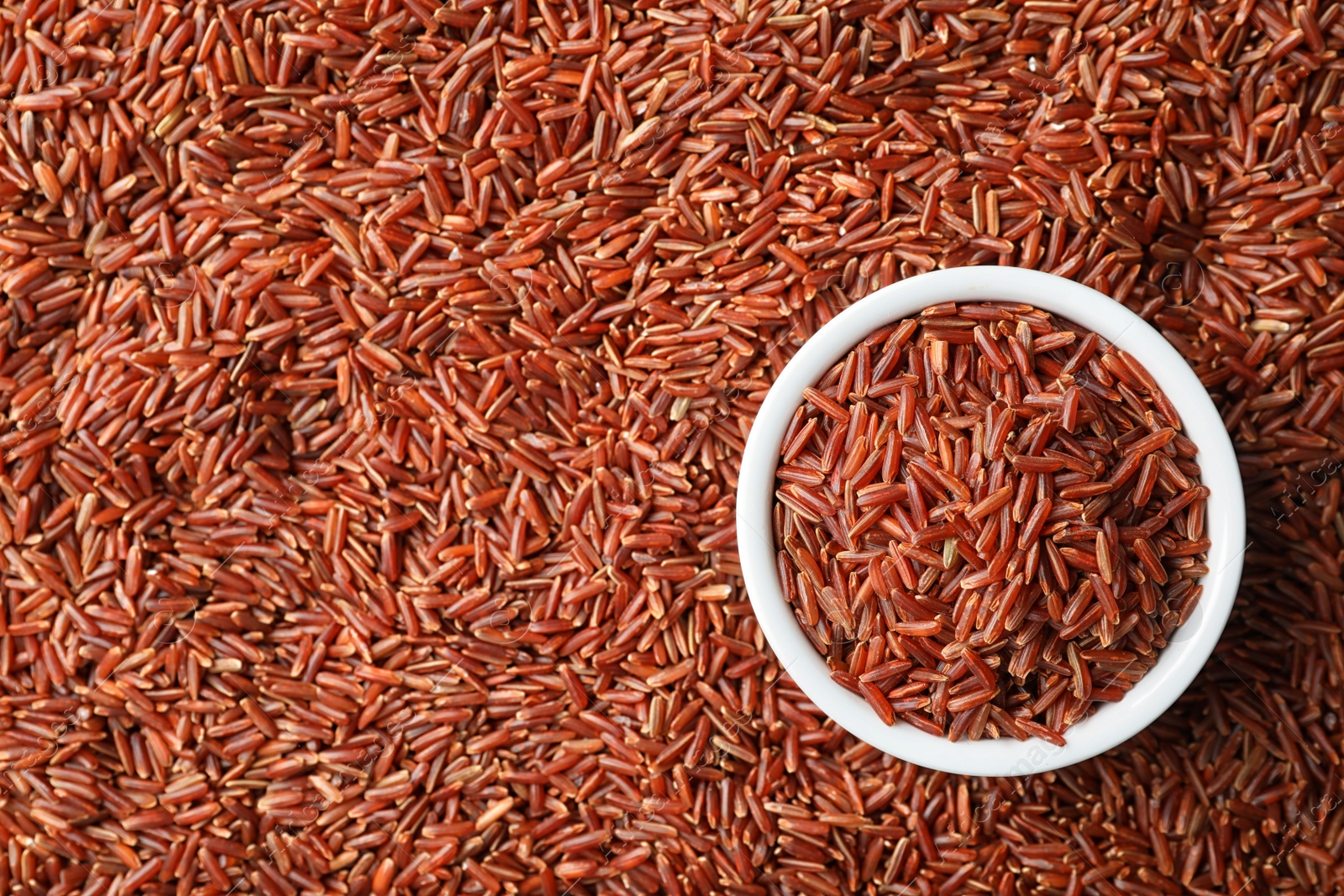 Photo of Ceramic bowl with cereal on raw brown rice, top view. Space for text