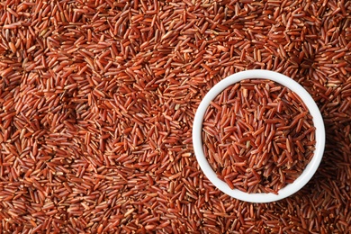 Photo of Ceramic bowl with cereal on raw brown rice, top view. Space for text