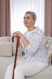 Senior woman with walking cane sitting on sofa at home