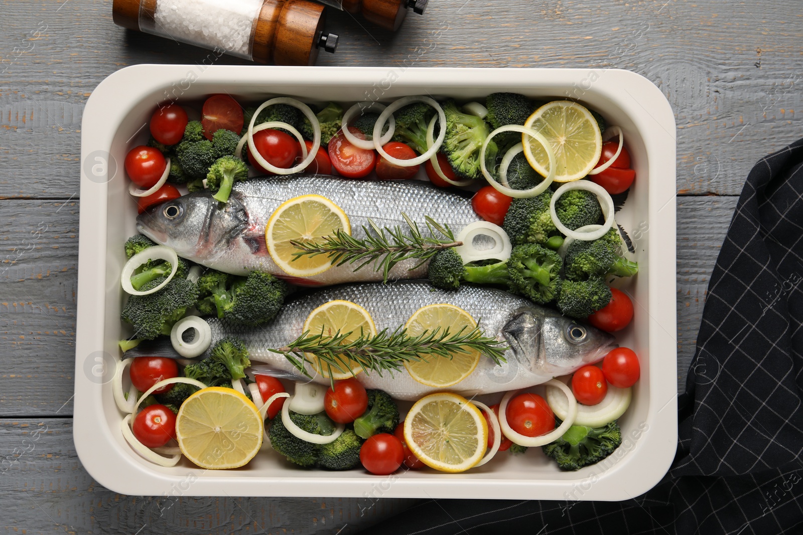 Photo of Raw fish with vegetables and lemon in baking dish on grey wooden table, top view