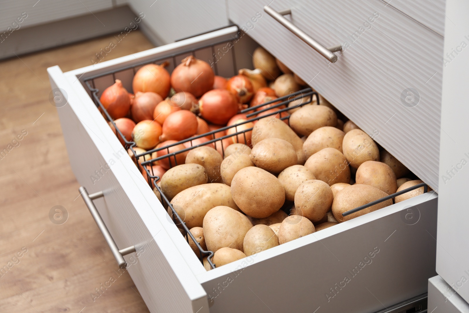 Photo of Open drawer with potatoes and onions in kitchen. Orderly storage