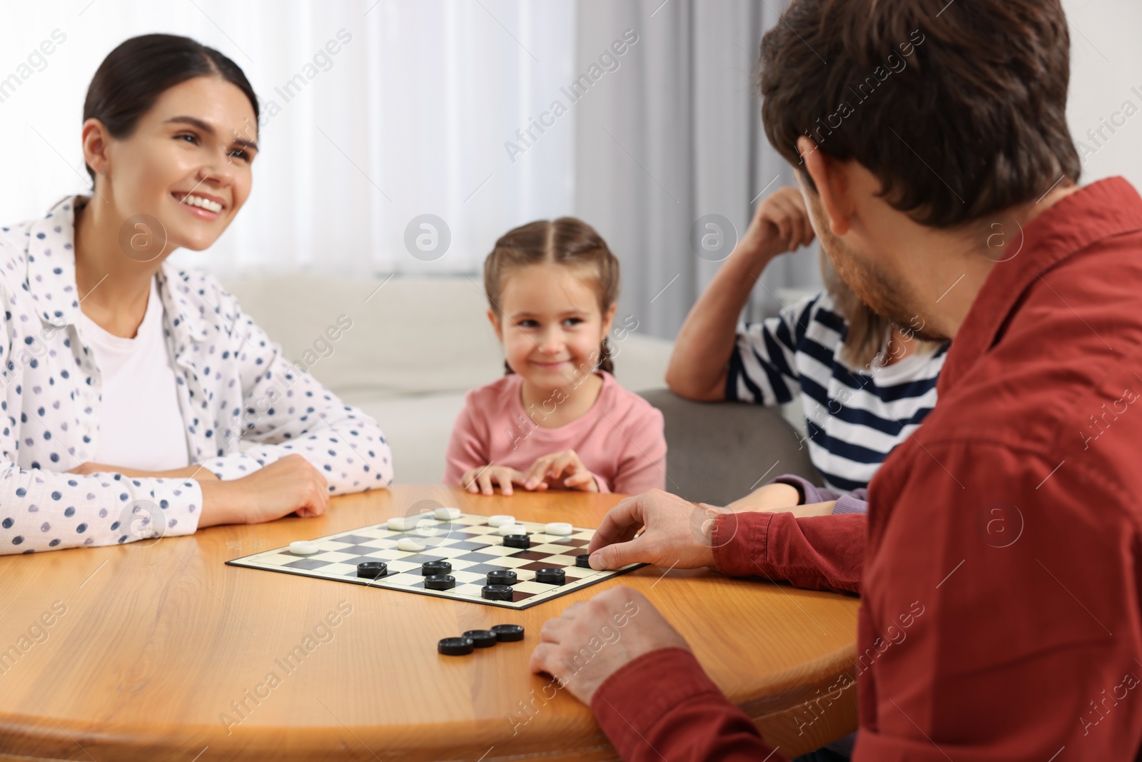 Photo of Family playing checkers at wooden table in room