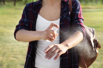 Photo of Woman applying insect repellent onto arm outdoors, closeup