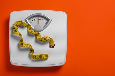 Weight loss concept. Scales and measuring tape on orange background, top view. Space for text