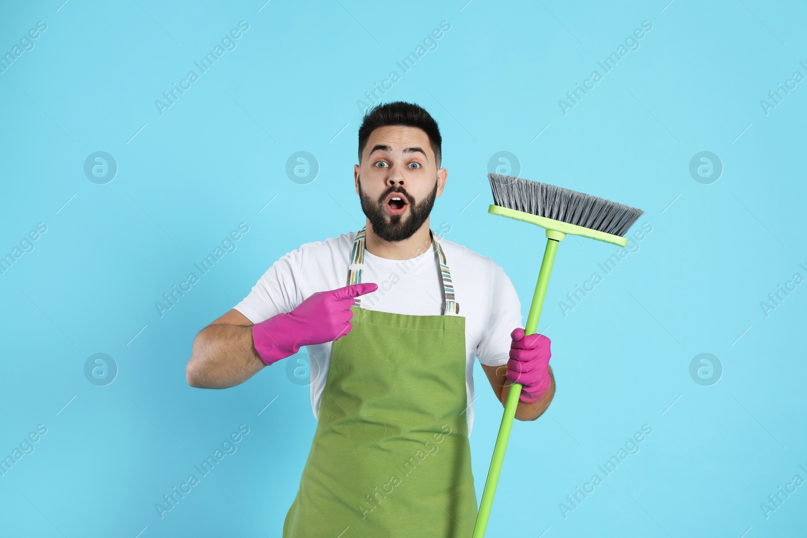 Photo of Emotional young man with green broom on light blue background