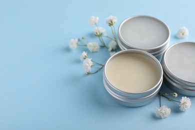 Different lip balms and gypsophila on light blue background, space for text