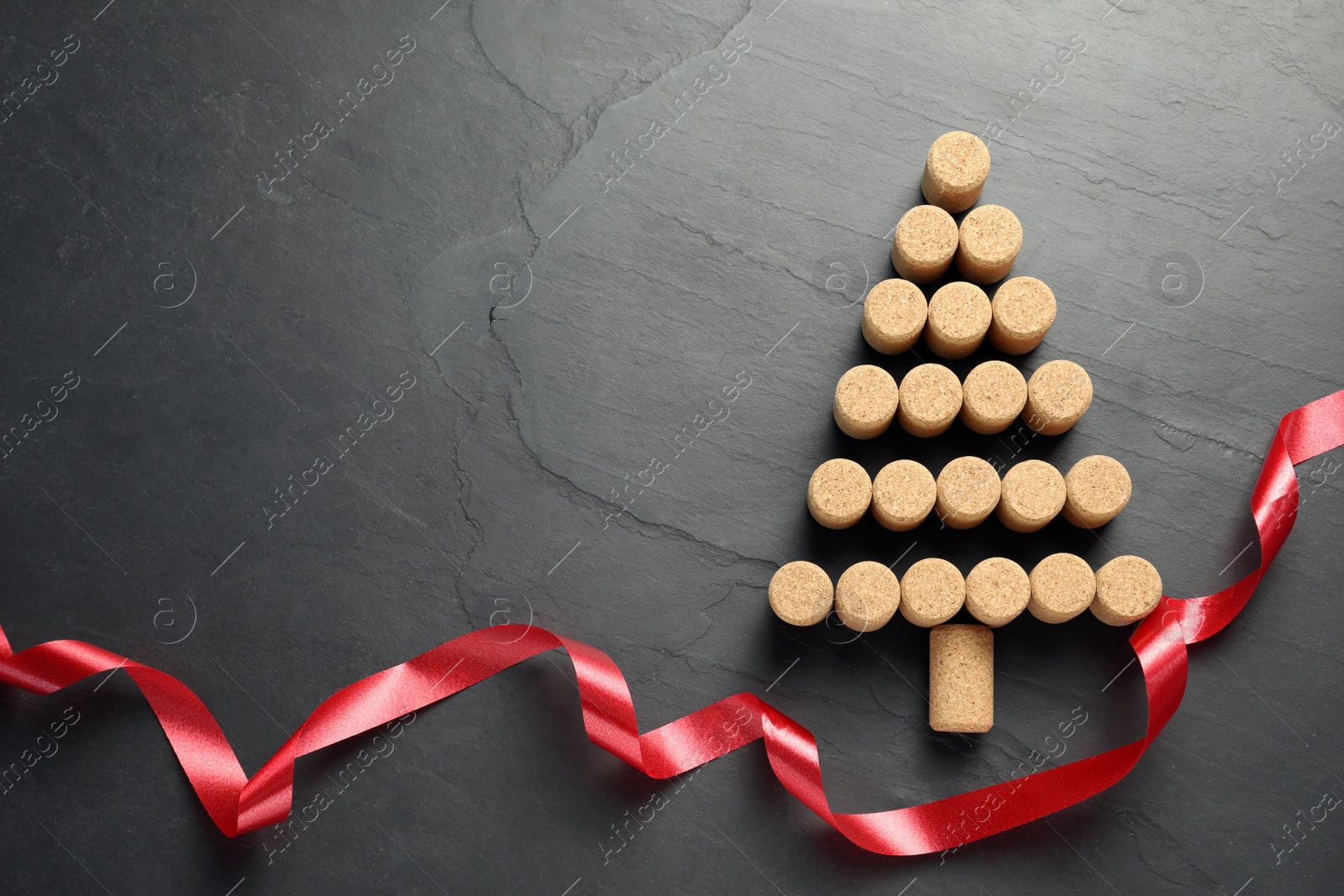 Photo of Christmas tree made of wine corks and red ribbon on dark stone background, top view. Space for text