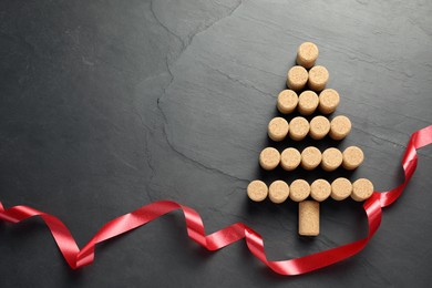 Christmas tree made of wine corks and red ribbon on dark stone background, top view. Space for text