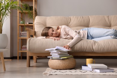 Photo of Young tired woman sleeping near books on couch at home