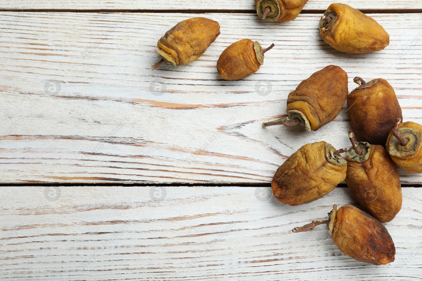 Photo of Many tasty dried persimmon fruits on white wooden table, flat lay. Space for text