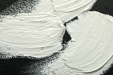 Photo of Strokes of white oil paint on black canvas, closeup