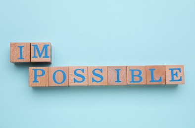 Motivation concept. Changing word from Impossible into Possible by removing wooden cubes on light blue background, flat lay