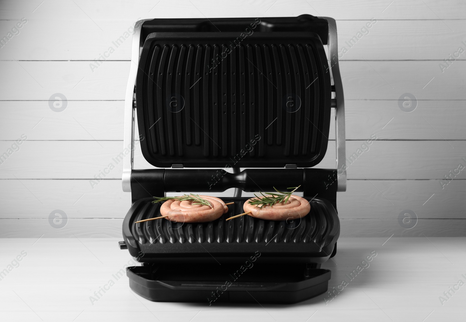 Photo of Electric grill with homemade sausages and rosemary on wooden table