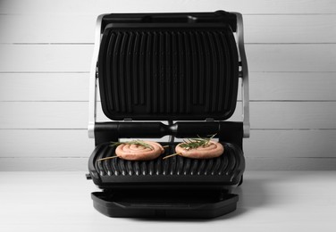 Electric grill with homemade sausages and rosemary on wooden table