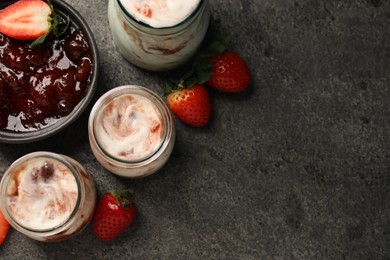 Tasty yoghurt with jam and strawberries on grey textured table, top view. Space for text