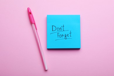 Paper note with phrase Don't Forget and pen on pink background, flat lay