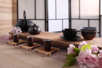 Photo of Beautiful set for traditional tea ceremony and sakura flowers on wooden table