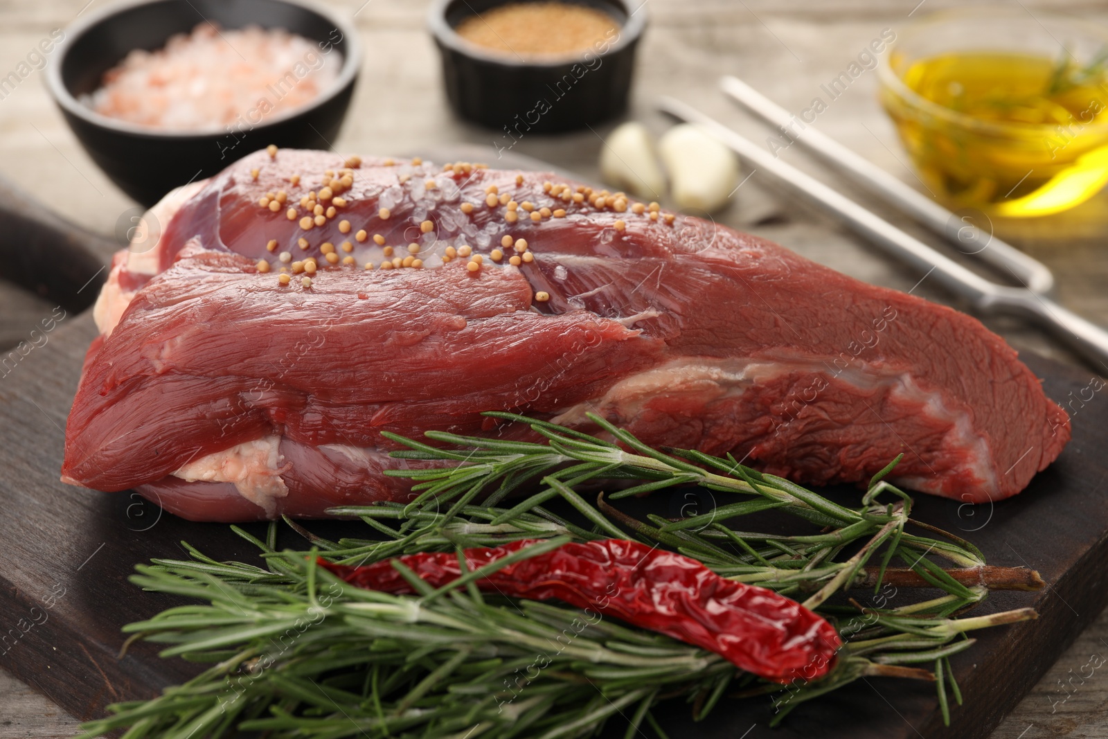 Photo of Piece of raw beef meat, rosemary, spices and chili pepper on table, closeup