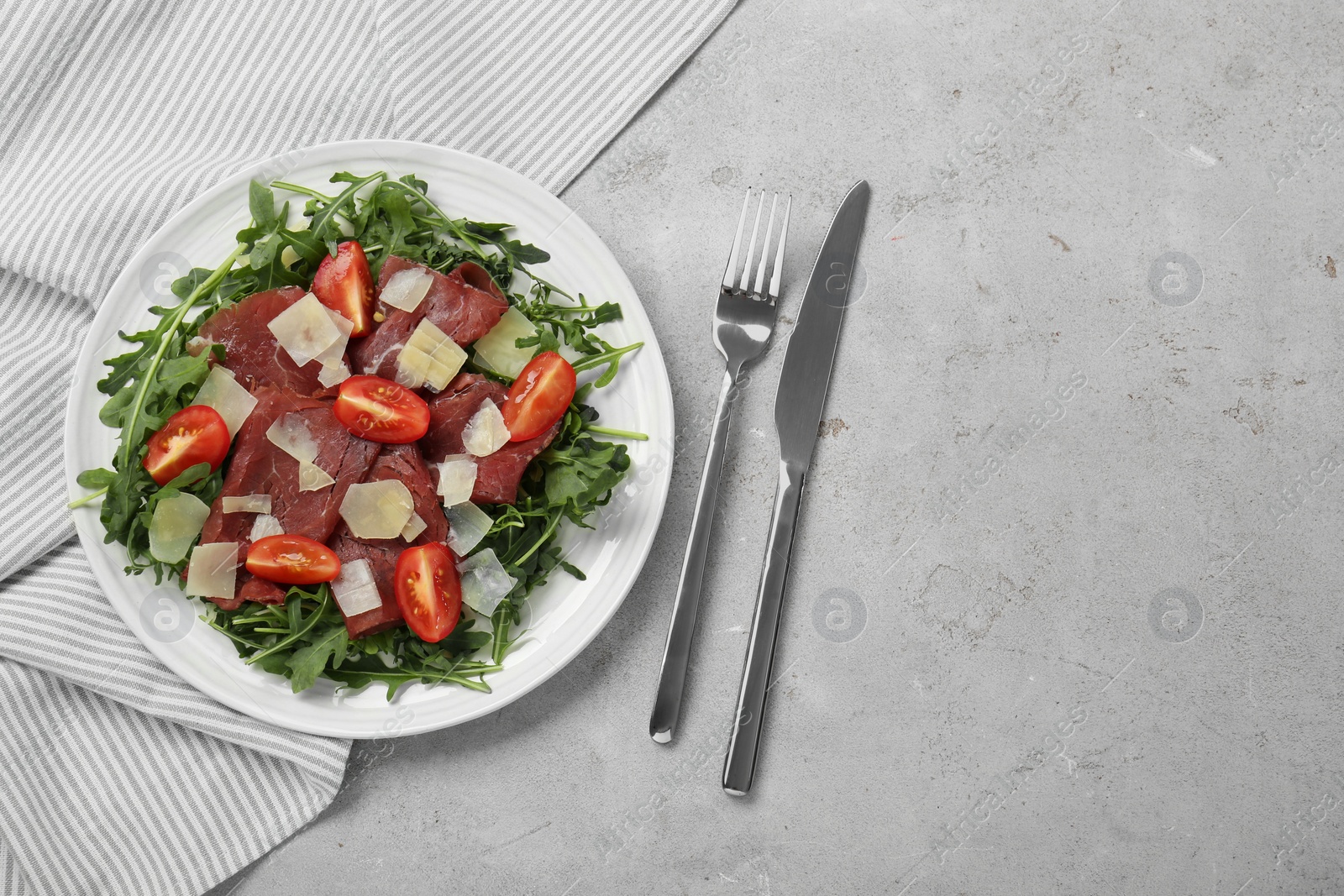 Photo of Delicious bresaola salad with parmesan cheese served on light grey textured table, flat lay. Space for text