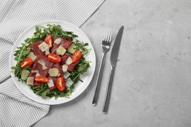 Photo of Delicious bresaola salad with parmesan cheese served on light grey textured table, flat lay. Space for text
