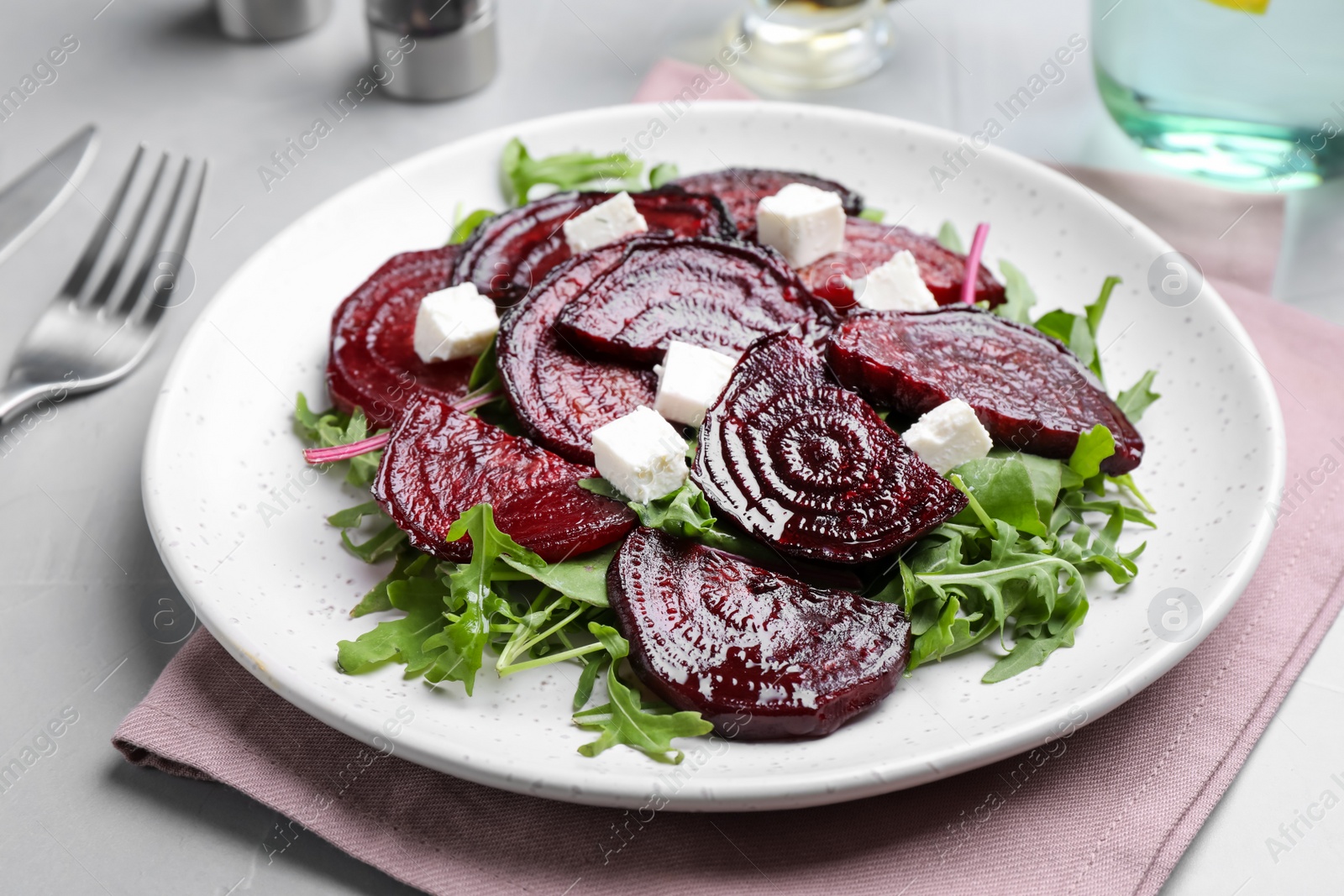 Photo of Roasted beetroot slices with feta cheese and arugula on light grey table, closeup