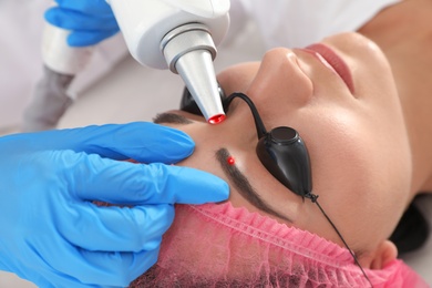 Photo of Woman undergoing laser tattoo removal procedure in salon, closeup