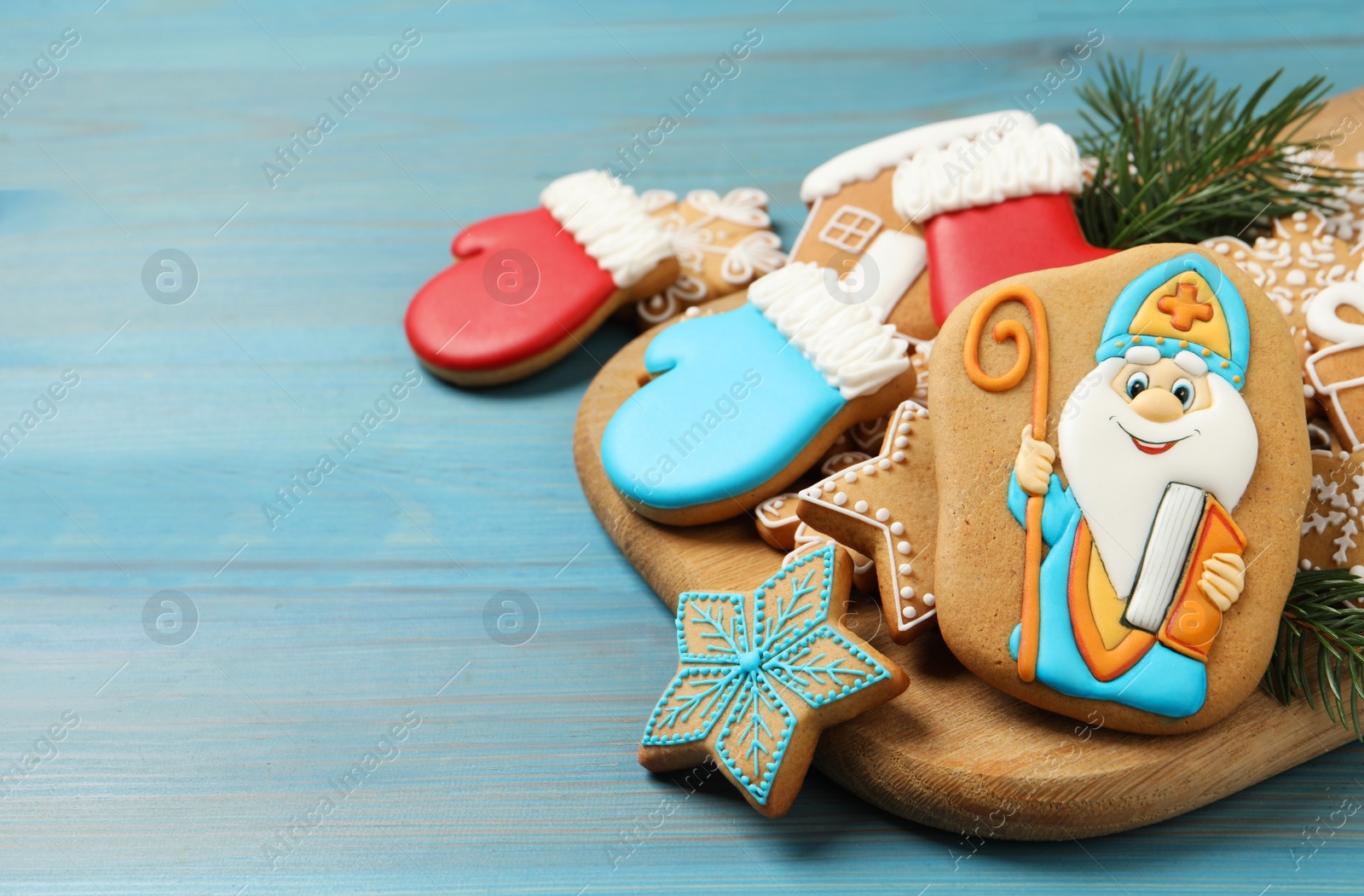 Photo of Tasty gingerbread cookies and fir branches on light blue wooden table, space for text. St. Nicholas Day celebration