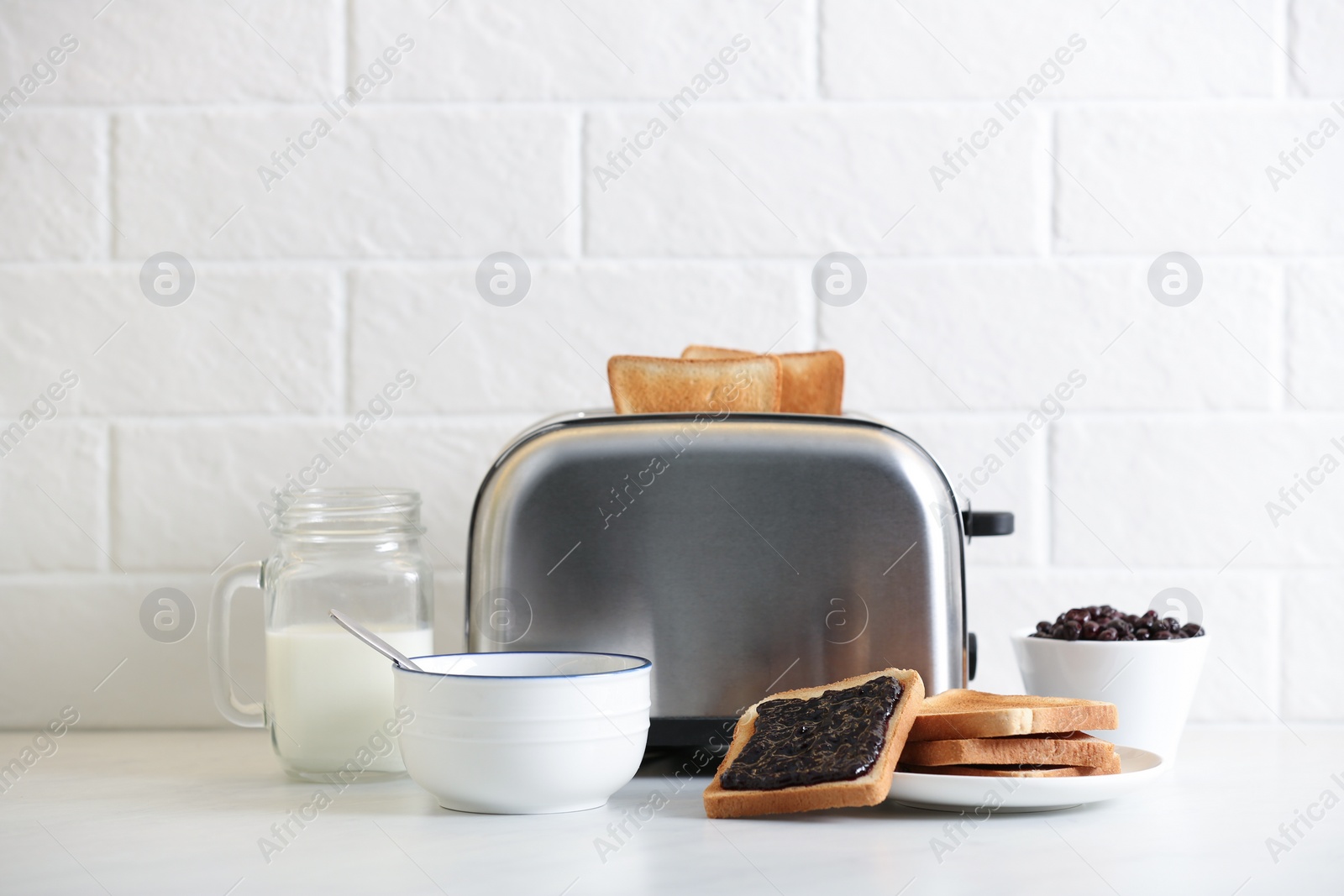 Photo of Modern toaster and delicious breakfast on table near brick wall