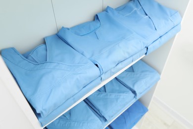 Photo of Light blue medical uniforms on white rack, above view