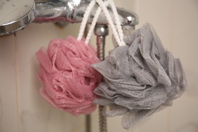 Photo of Colorful shower puffs hanging on faucet in bathroom, closeup