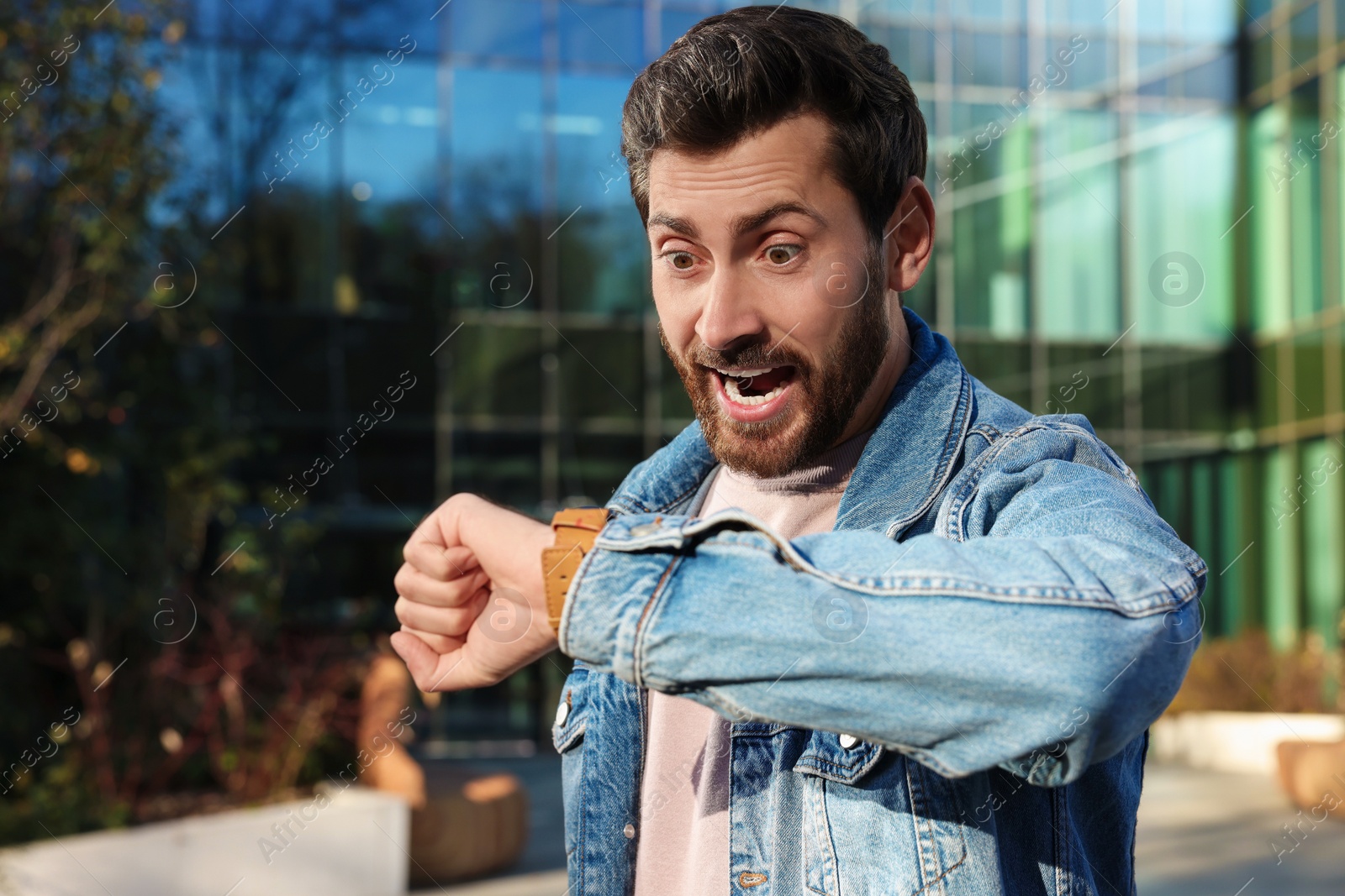 Photo of Emotional man checking time on watch near building. Being late concept