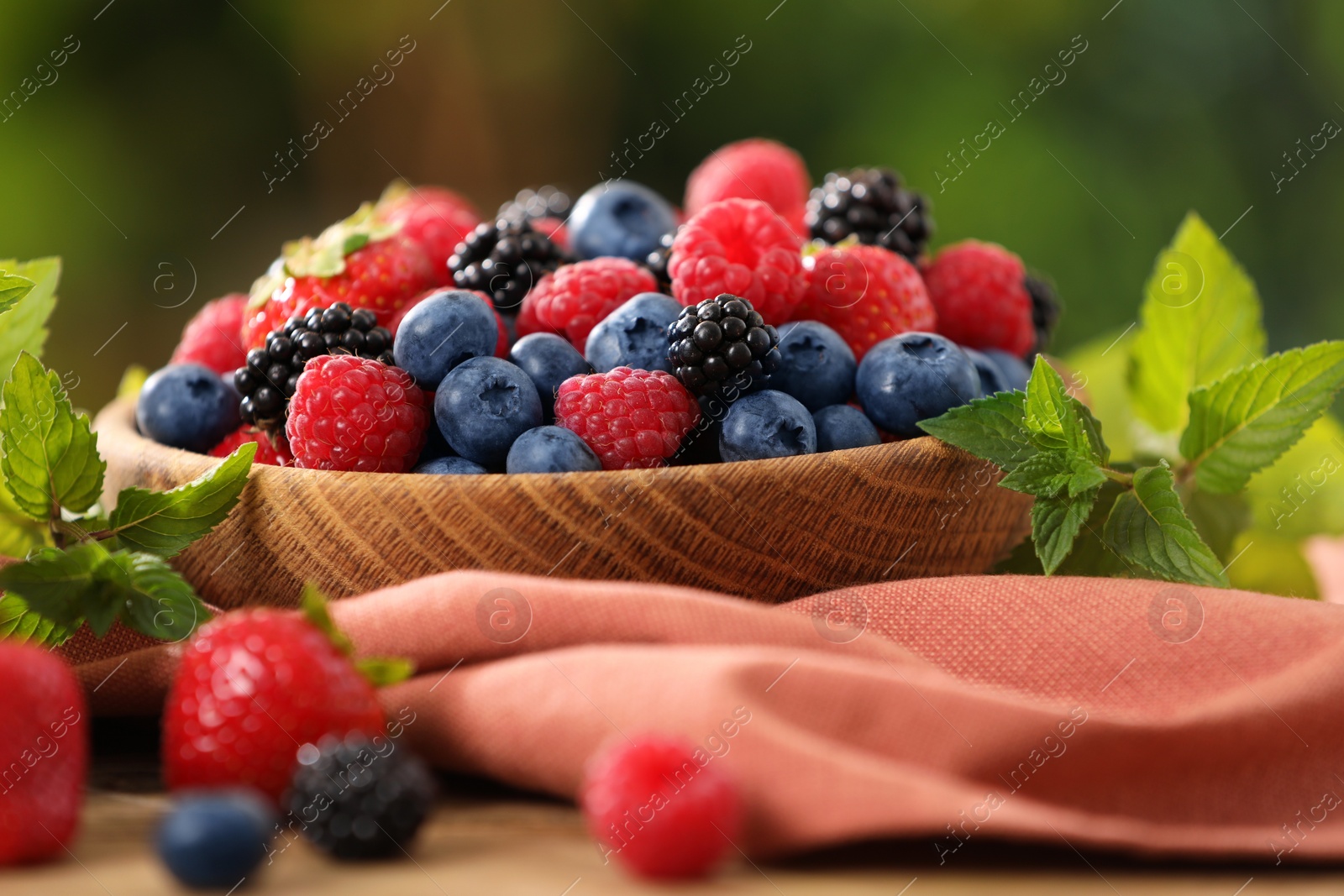 Photo of Bowl with different fresh ripe berries and mint on table outdoors, closeup