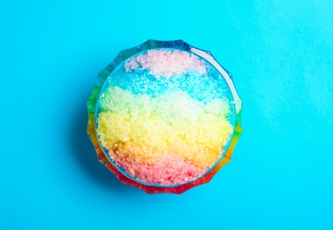 Rainbow shaving ice in glass dessert bowl on light blue background, top view