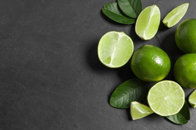 Photo of Fresh ripe limes and leaves on black table, top view. Space for text