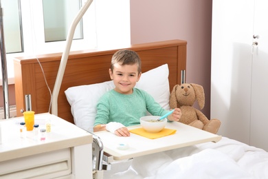 Little child with intravenous drip eating soup in hospital bed