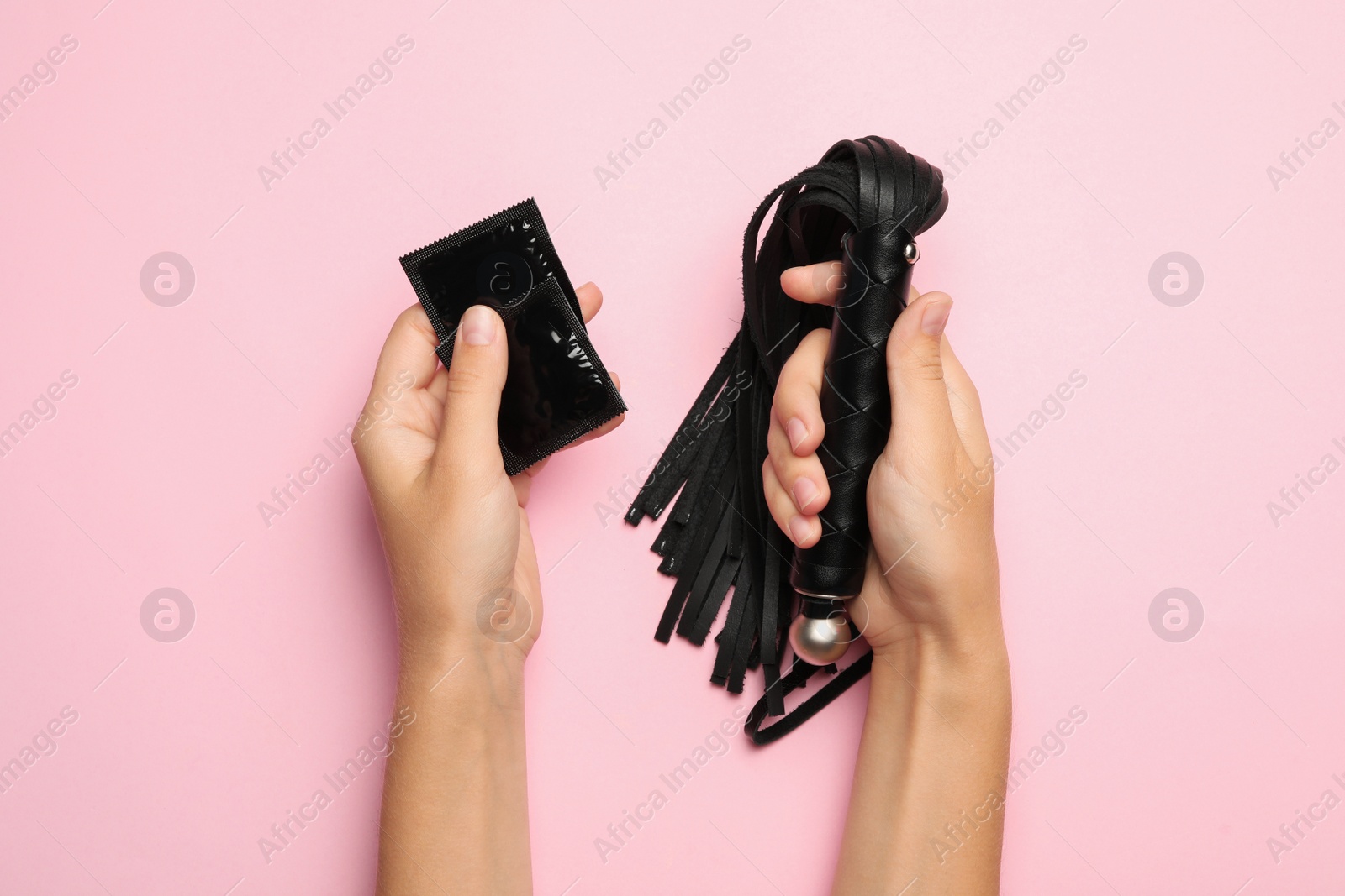 Photo of Woman with whip and condoms on pink background, top view. Sex game