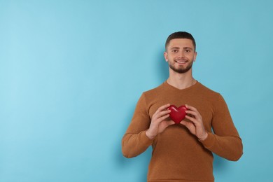 Happy volunteer holding red heart with hands on light blue background. Space for text