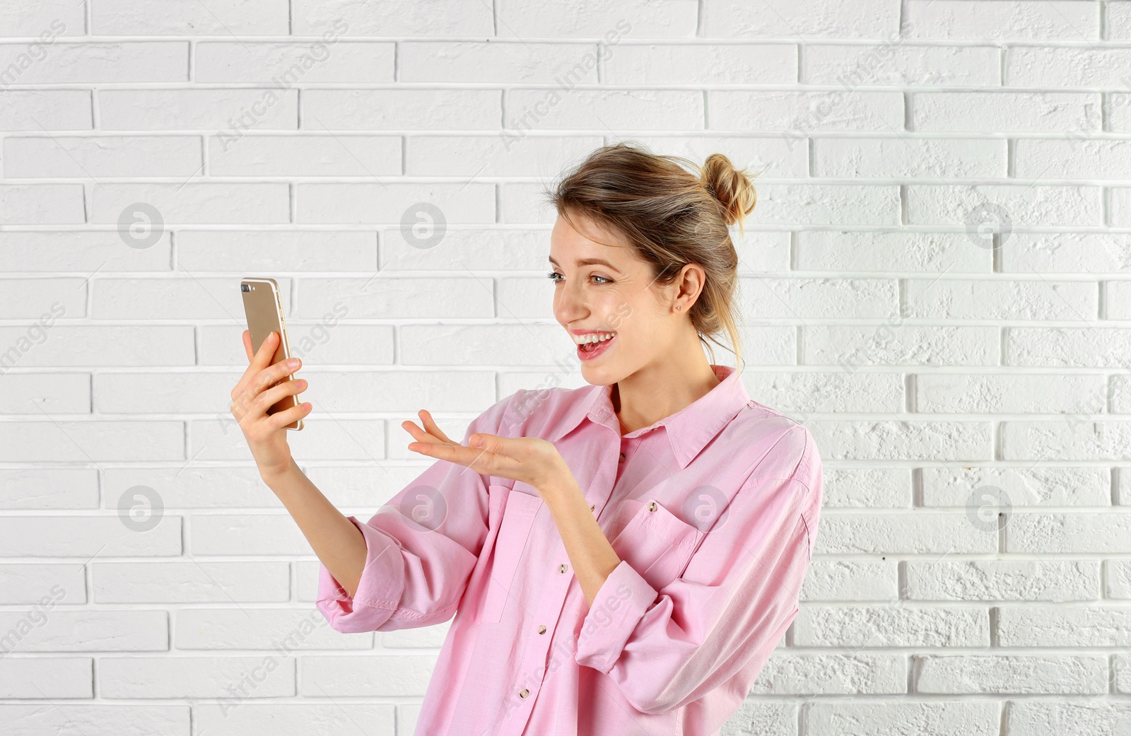 Photo of Woman using mobile phone for video chat against brick wall