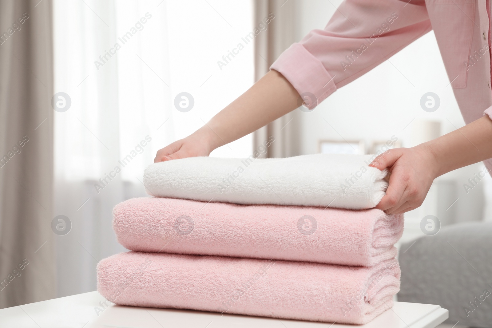 Photo of Woman stacking clean towels on table in room