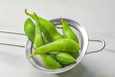 Photo of Sieve with green edamame beans in pods on white table, closeup
