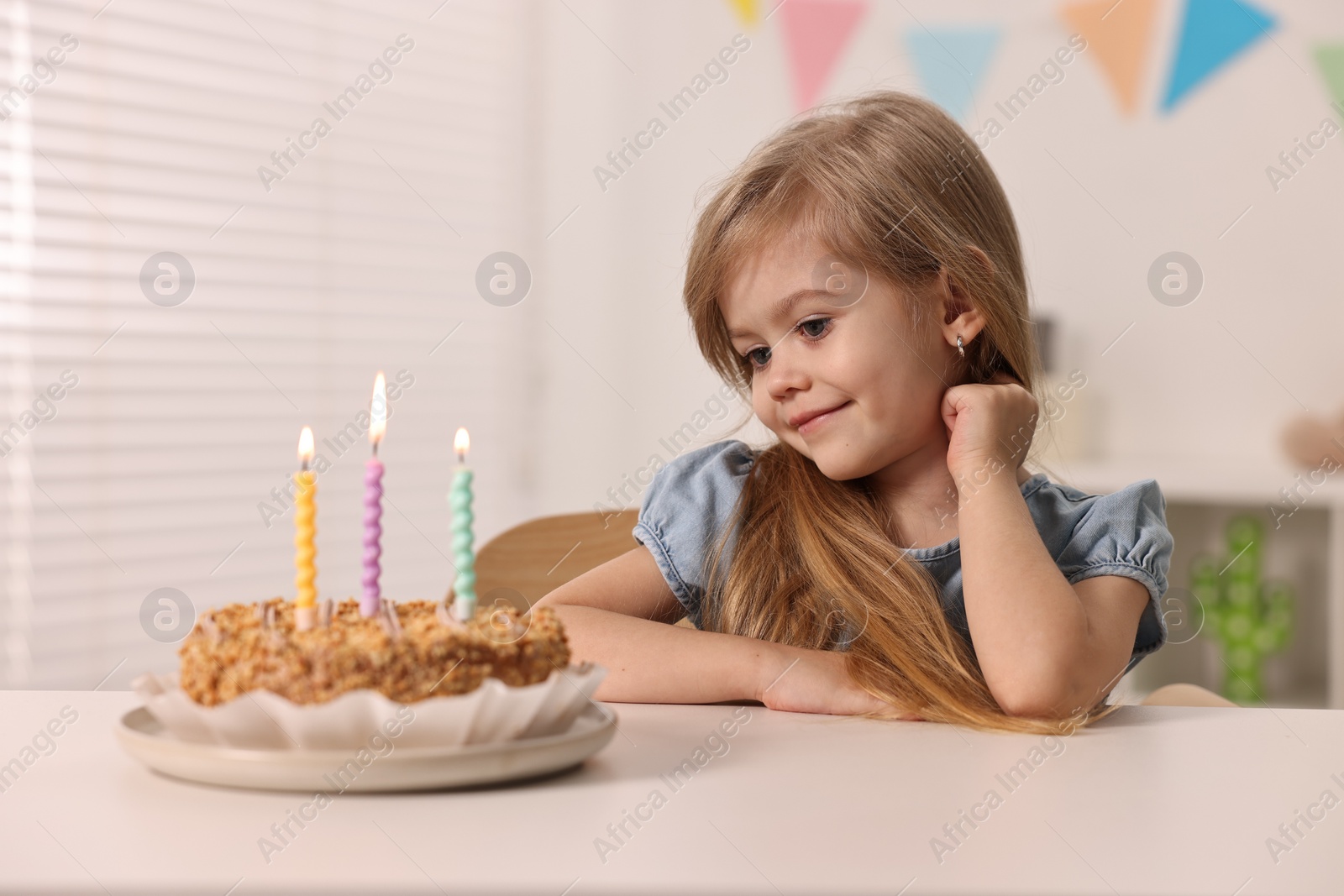 Photo of Cute girl with birthday cake at table indoors