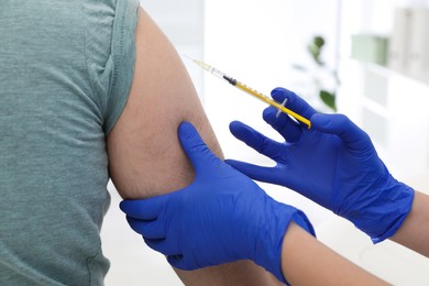 Doctor giving injection to man in hospital, closeup. Immunization concept