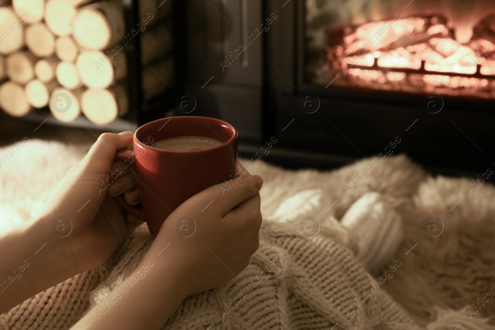 Photo of Woman with hot drink resting near fireplace at home, closeup