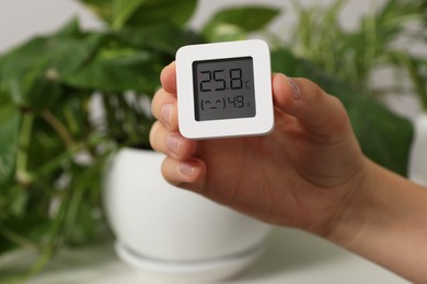 Photo of Woman holding digital hygrometer with thermometer on blurred background, closeup
