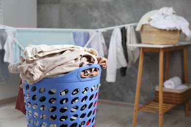 Photo of Plastic laundry basket overfilled with clothes indoors. Space for text